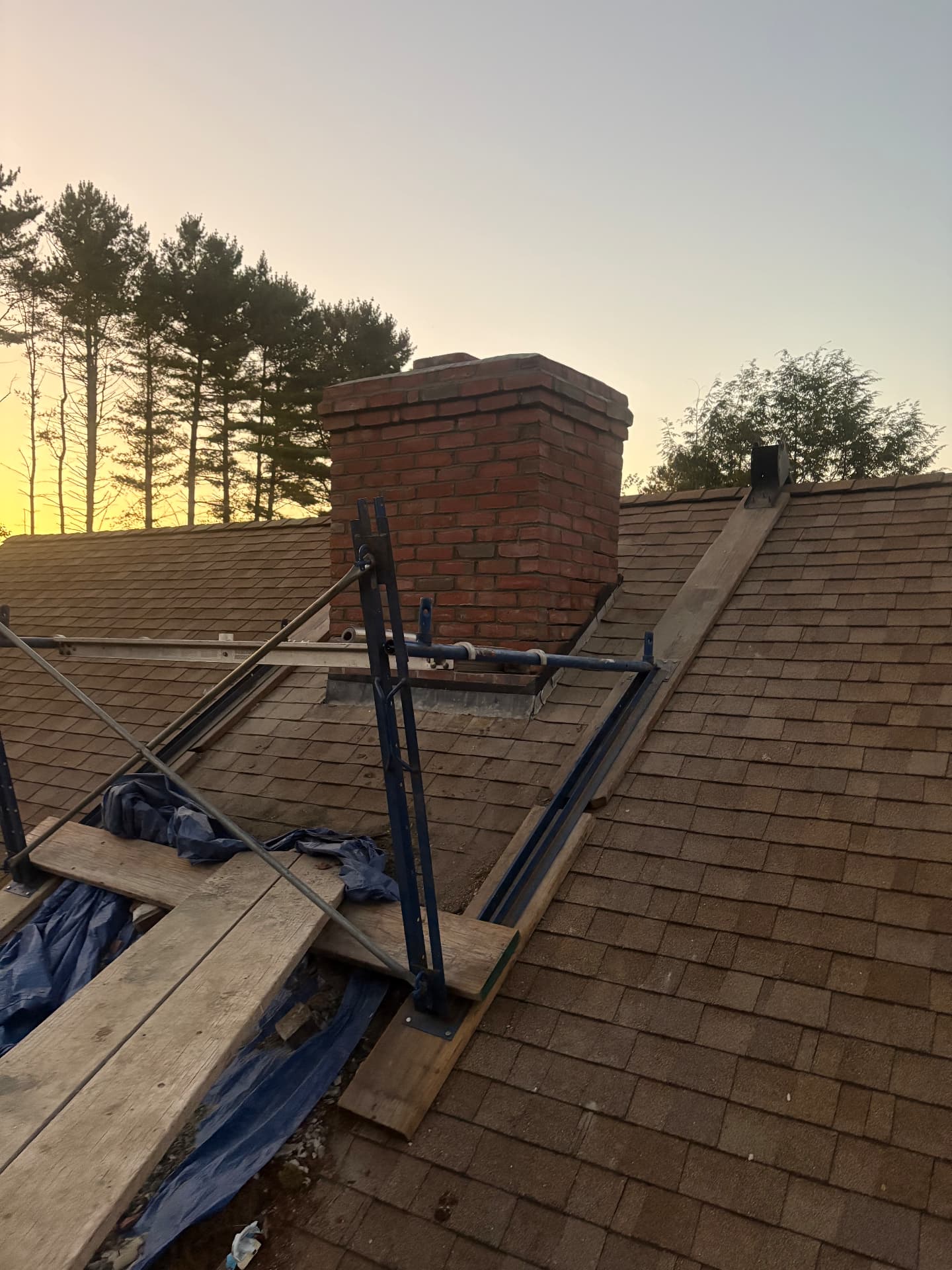 Brick chimney rebuild at sunset with roof staging in place