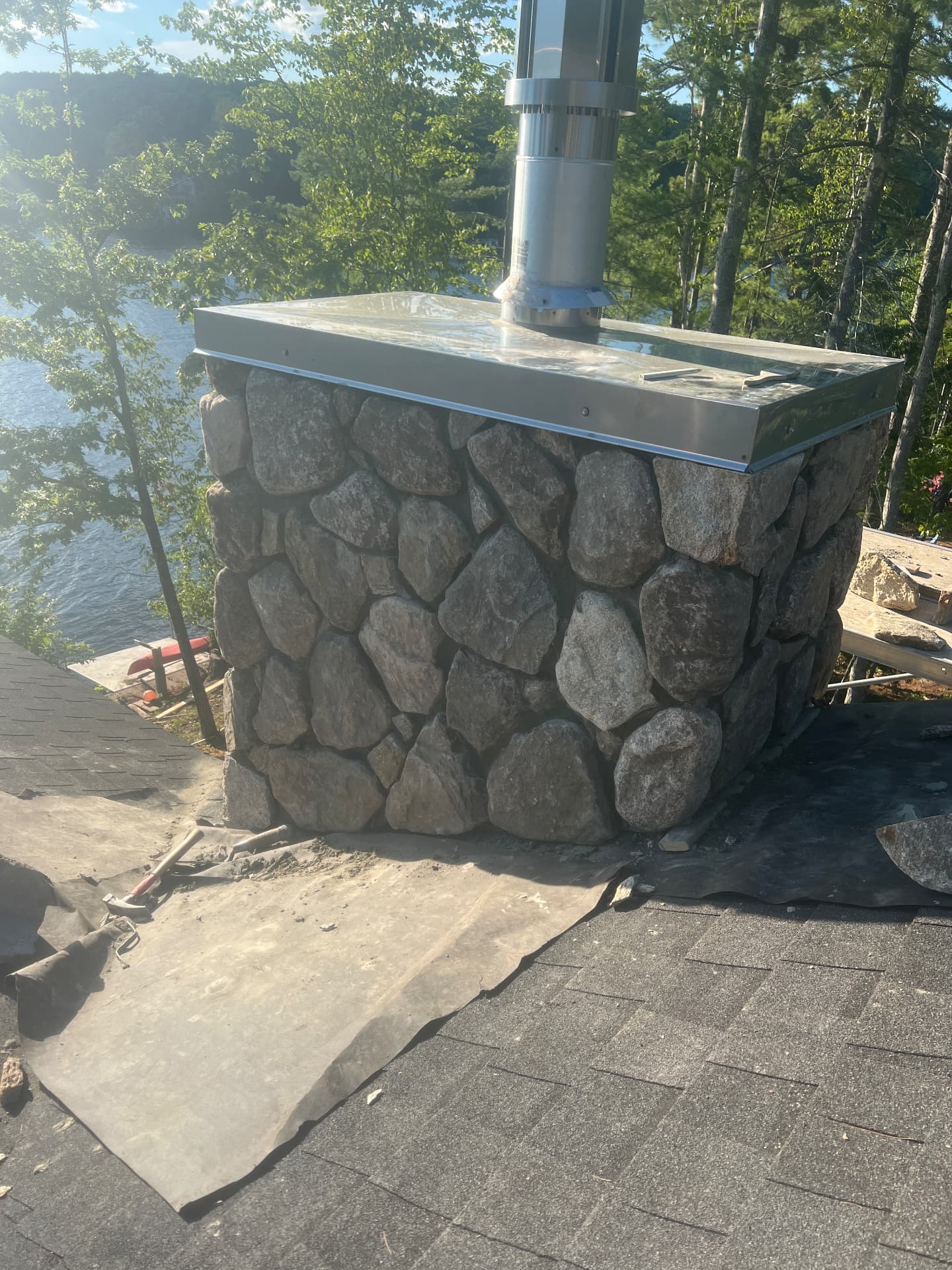 Natural stone chimney with stainless cap above a lake